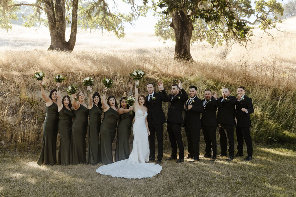 Wedding couple and bridal party standing next to each other celebrating with golden field behind them at French Oak Ranch