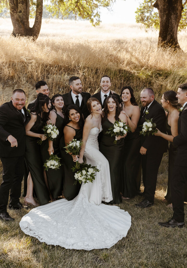Wedding couple laughing and joking around with bridal party while looking at camera with golden field behind them at French Oak Ranch