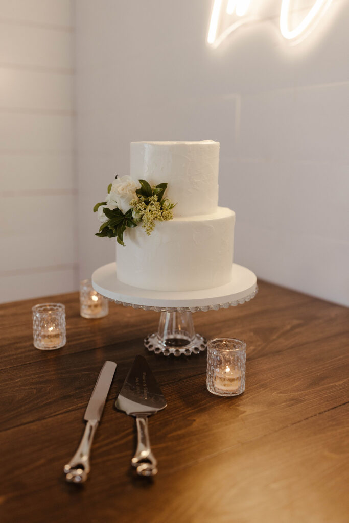 Wedding cake on white pedestal with candles around it and white floral decor on French Oak Ranch
