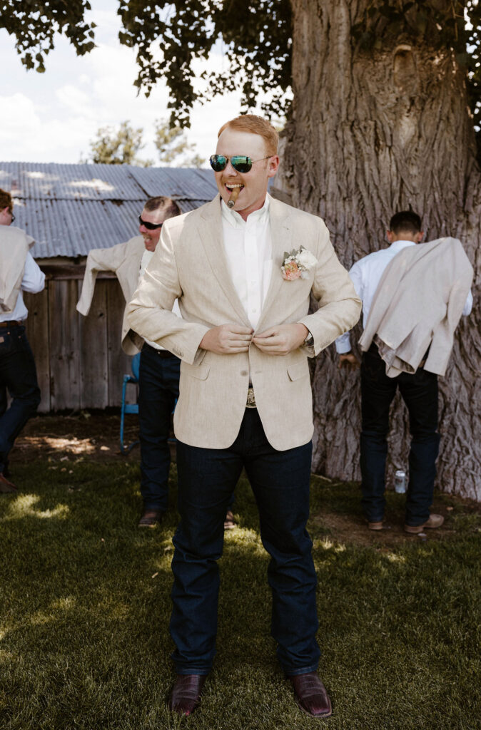 Wedding groom buttoning jacket with cigar in mouth and groomsmen behind him at Jacobs Berry Farm