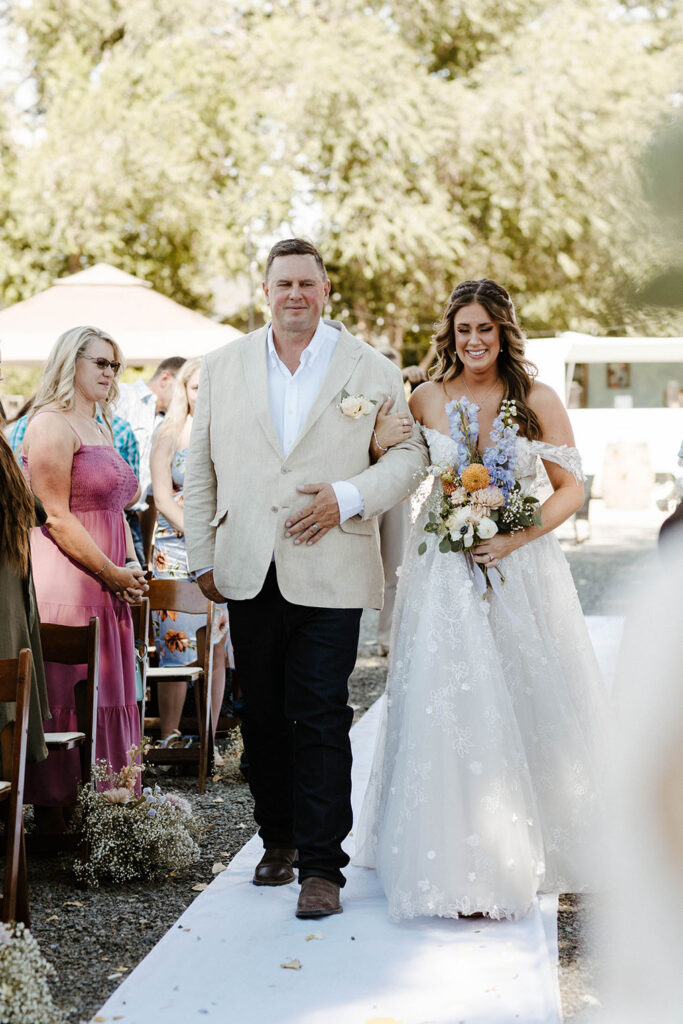 Bride emotional and smiling while walking down wedding aisle holding dad's arm during ceremony at Jacobs Berry Farm