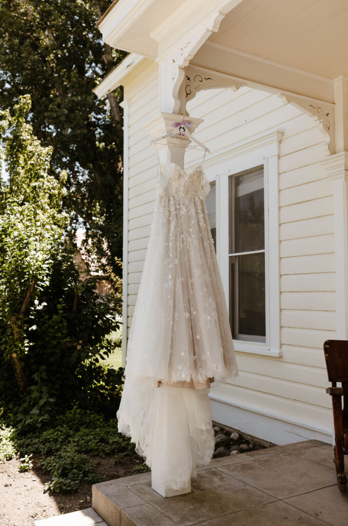 Wedding dress hanging on white pillar outside on patio with house in background at Jacobs Berry Farm