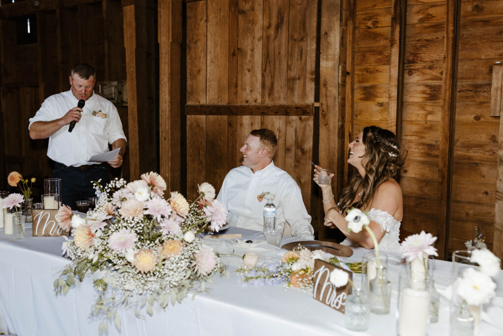 Wedding couple having drinks while sitting at reception and listening to speeches with big floral bouquet on table at Jacobs Berry Farm