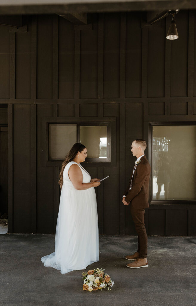 Bride reading wedding vows to groom while he stands with his hands clasped in front of him at the Coachman hotel in Lake Tahoe