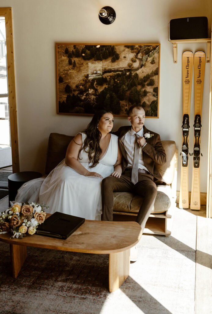 Wedding couple sitting on couch together while looking out window with skis and painting behind them at the Coachman Hotel in Lake Tahoe