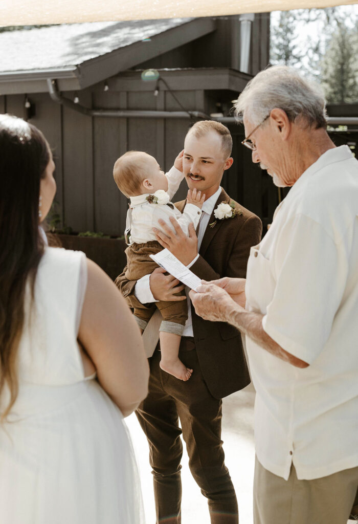 Baby playing with groom's face while officiant is reading during wedding ceremony at the Coachman hotel in Lake Tahoe