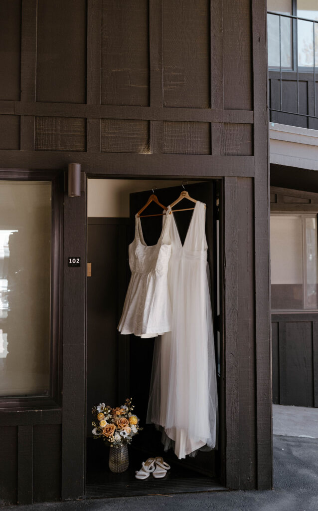 Bride's wedding dress and reception outfit on wooden hangars hanging next to each other in doorway at the Coachman hotel in Lake Tahoe