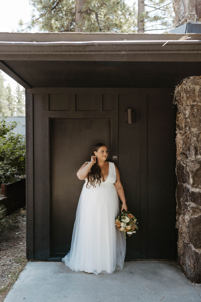 Wedding bride holding brown and white floral bouquet while playing with hair in front of dark brown building at the coachman hotel in Lake Tahoe
