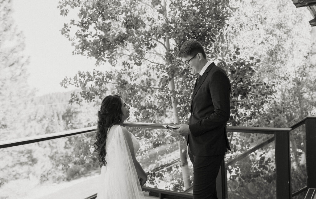 Wedding groom reading vows to bride while next to wooden railing outside at the Tannenbaum