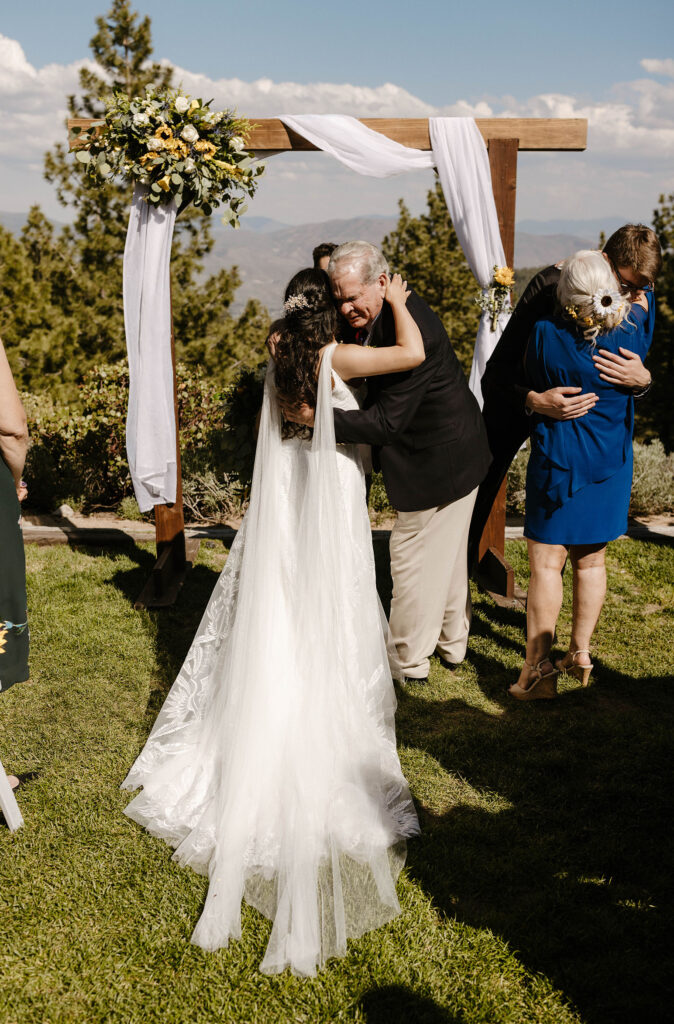 Wedding bride and dad hugging at ceremony with arch in background with sunflowers at the Tannenbaum