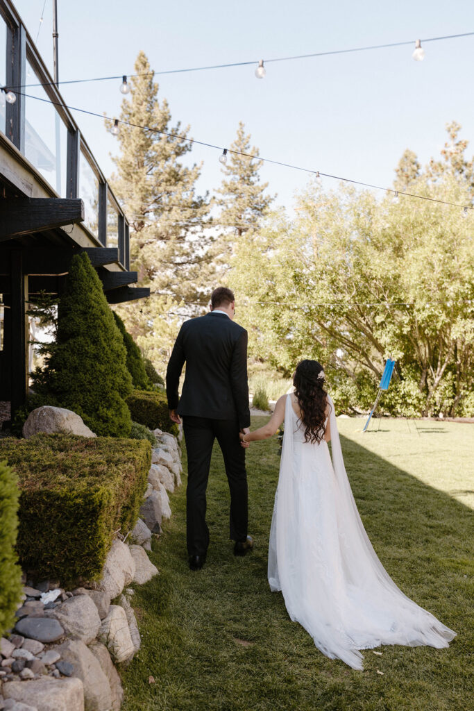 Wedding couple holding hands and walking away from camera together on grass next to rocks at the Tannenbaum