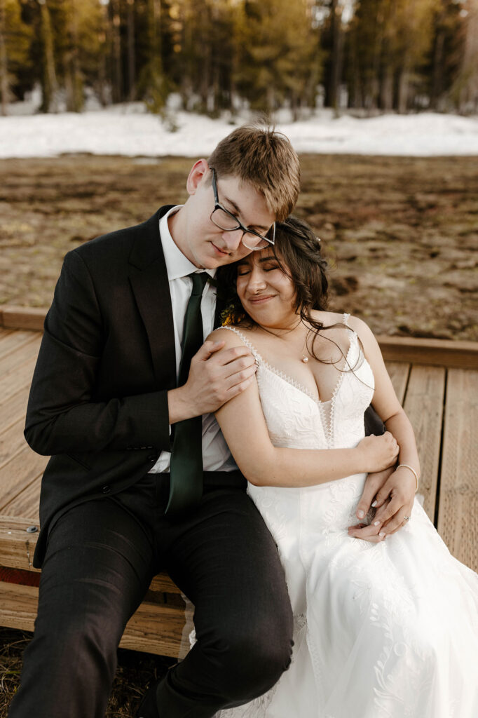 Wedding couple sitting on wooden walkway together while leaning into each other at the Tannenbaum