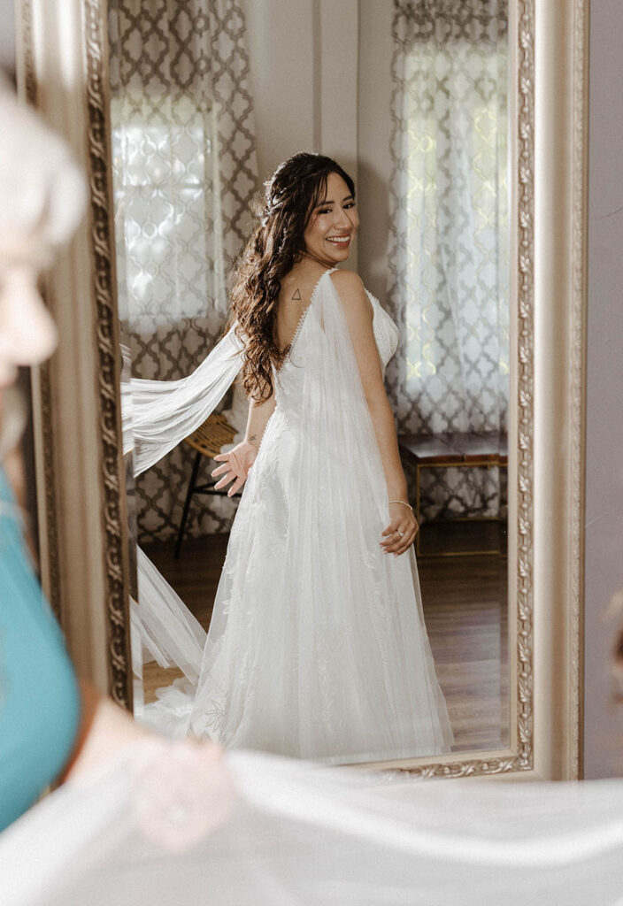 Bride looking at wedding dress in large mirror while twirling it inside at the Tannenbaum