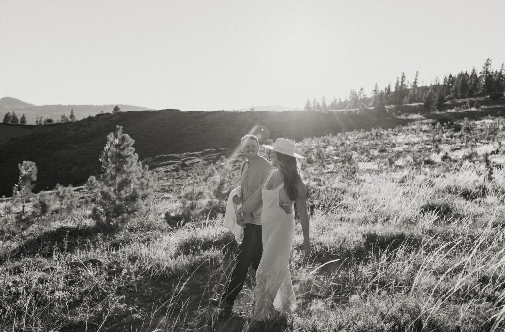 Man smiling at wife while they hold hands and walk down hill together with pine trees in background at Donner Lake