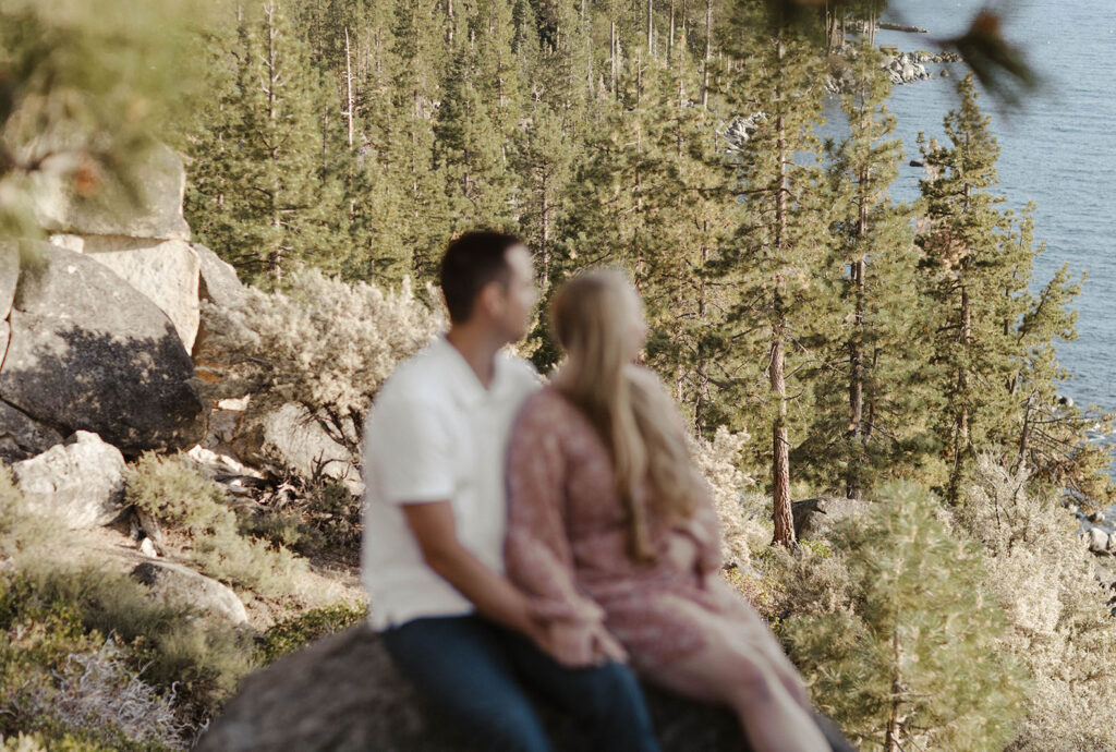 couple sitting on a rock together blurry with lake tahoe in focus