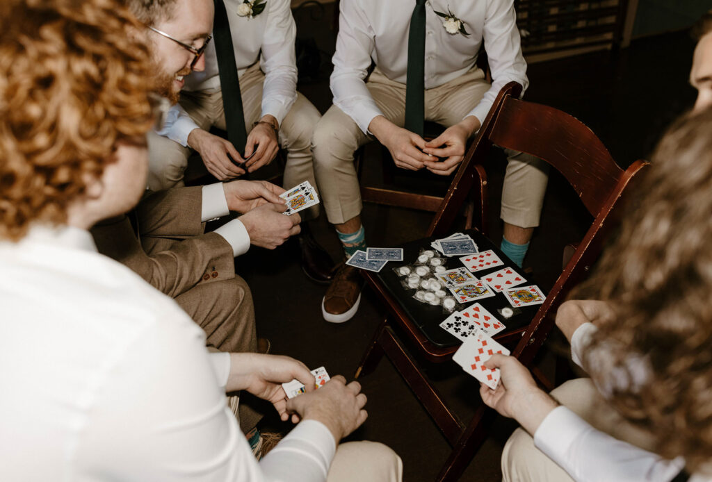 Wedding groom and groomsmen sitting and playing cards while getting ready inside at Valhalla in Lake Tahoe