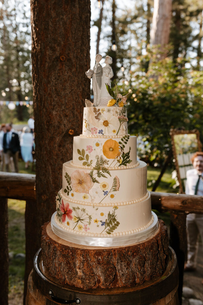 Wedding cake with colorful flowers and couple figurine on top of wooden plate at Valhalla in Lake Tahoe