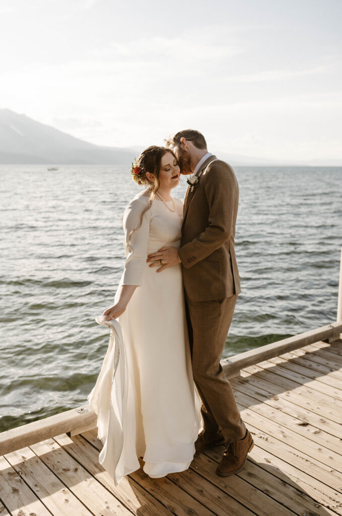 Wedding groom kissing brides cheek as they stand on wooden pier with Lake Tahoe in background