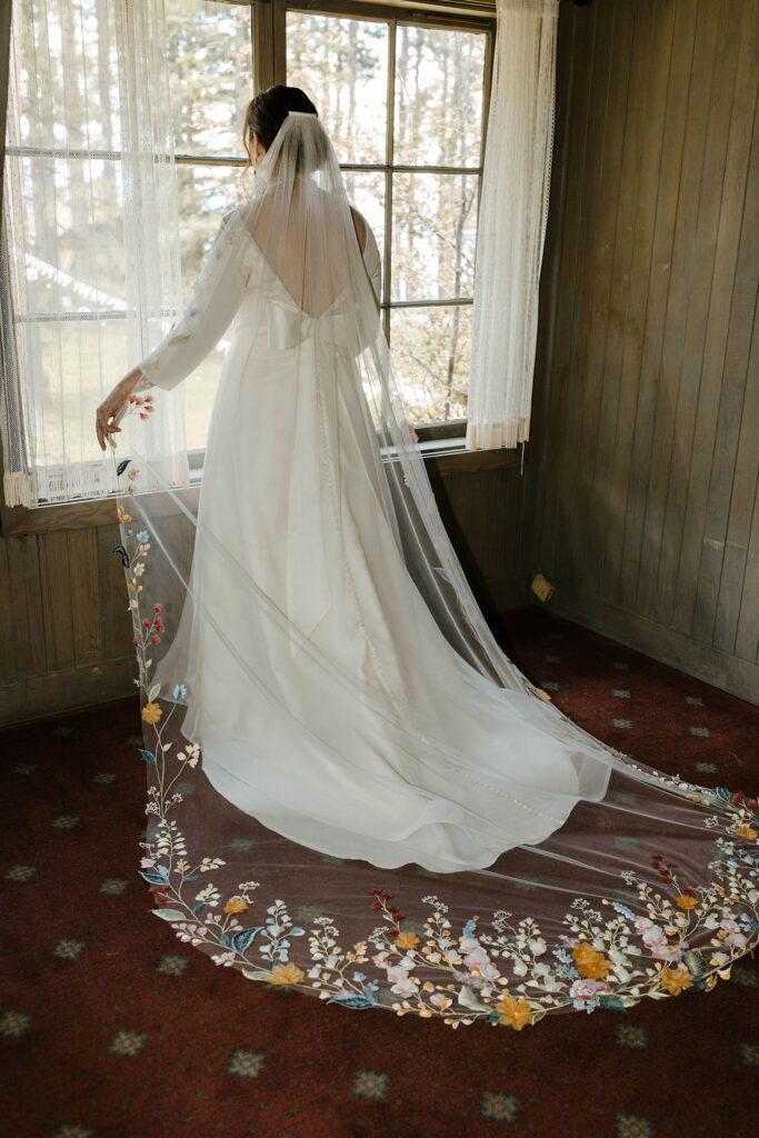Bride standing at window as wedding veil with colorful flowers trails behind her at Valhalla in Lake Tahoe