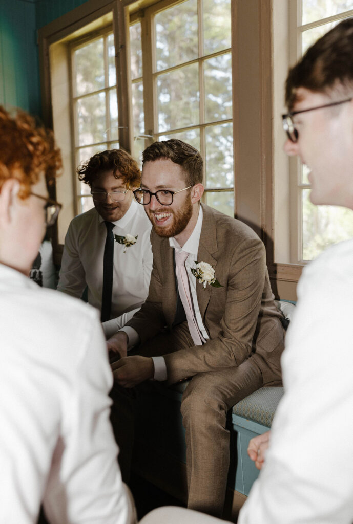 Wedding groom smiling while sitting around groomsmen inside at Valhalla in Lake Tahoe