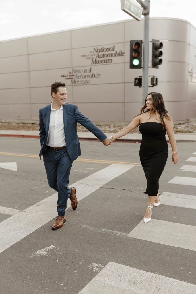 Couple holding hands while walking across the street together and smiling at each other in downtown Reno