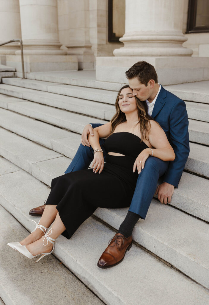 Woman sitting in between man's legs while he sits on concrete steps and kisses her cheek in downtown Reno