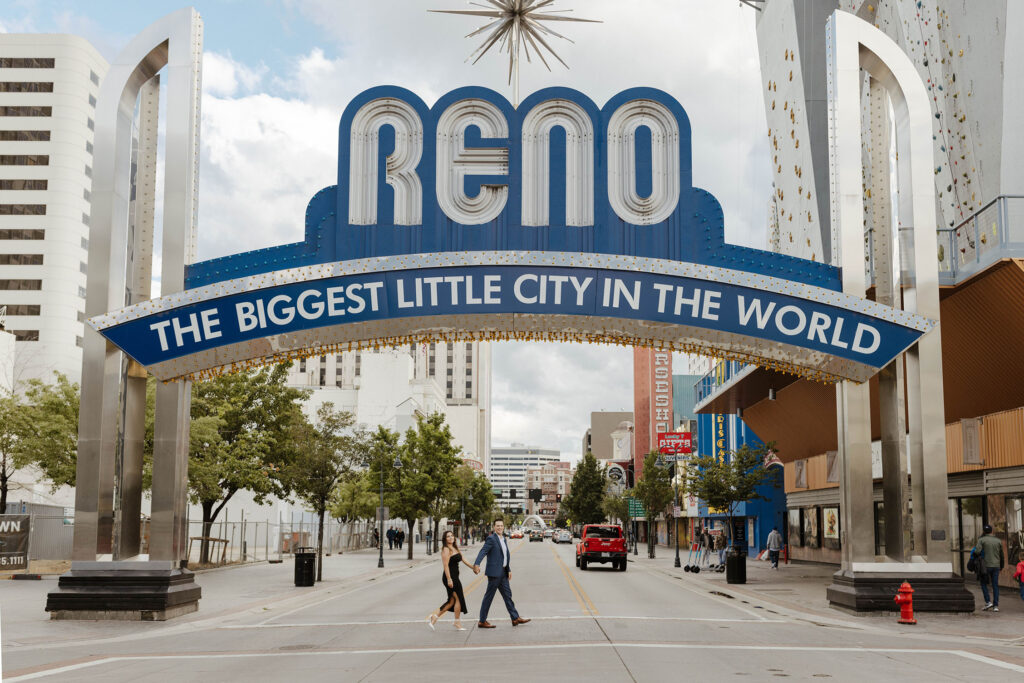 Engagement couple holding hands while walking under Reno's "biggest little city" sign