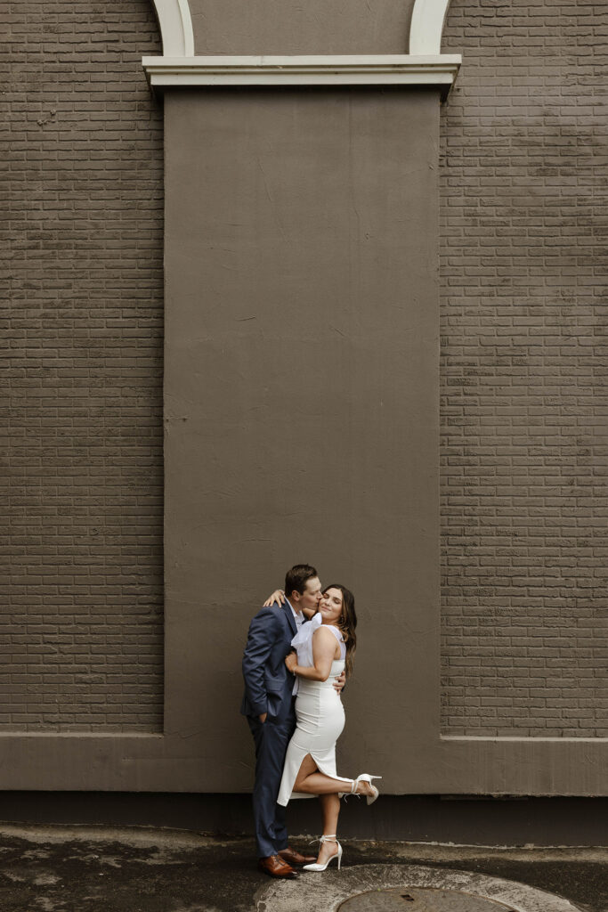 Man kissing woman on cheek while she smiles and both are standing in front of building in downtown reno