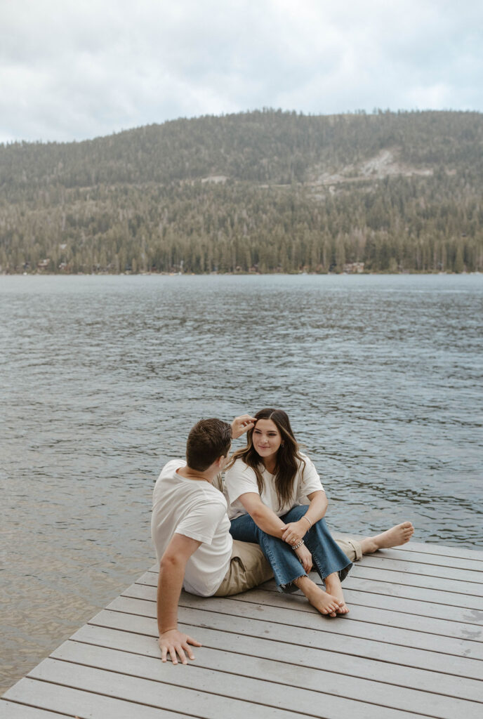 Engagement coupe sitting together on a pier in Lake Tahoe while man moves hair out of fiancé's face