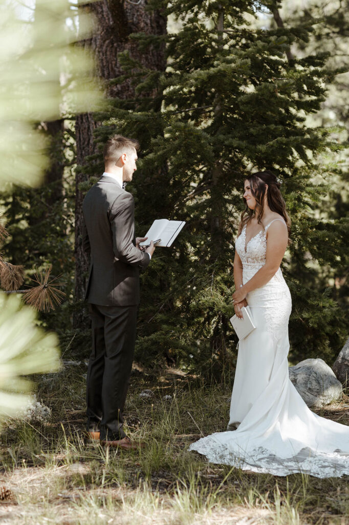 Groom reading wedding vows to bride while surrounded by pine trees at dancing pines