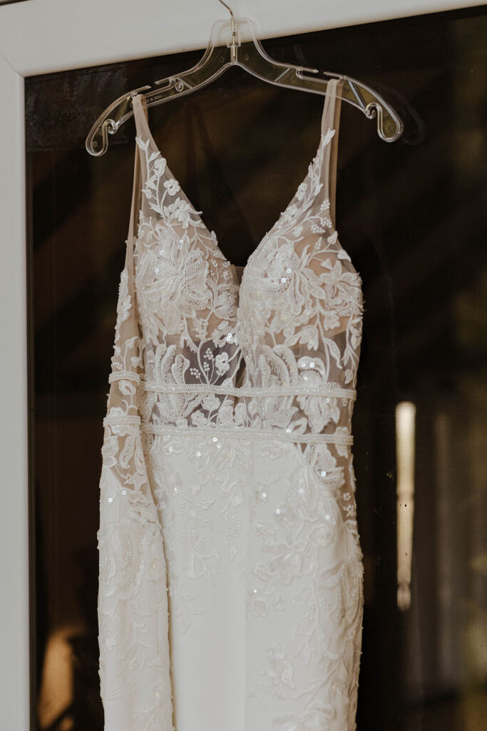 Lace wedding dress hanging in front of large window at dancing pnes