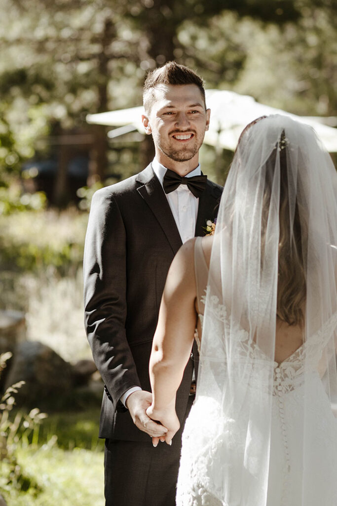 Groom holding hands and smiling at bride during wedding ceremony at dancing pines