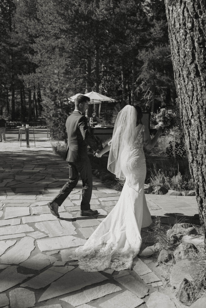 Wedding couple holding hands and walking away from ceremony at dancing pines on stone pathway