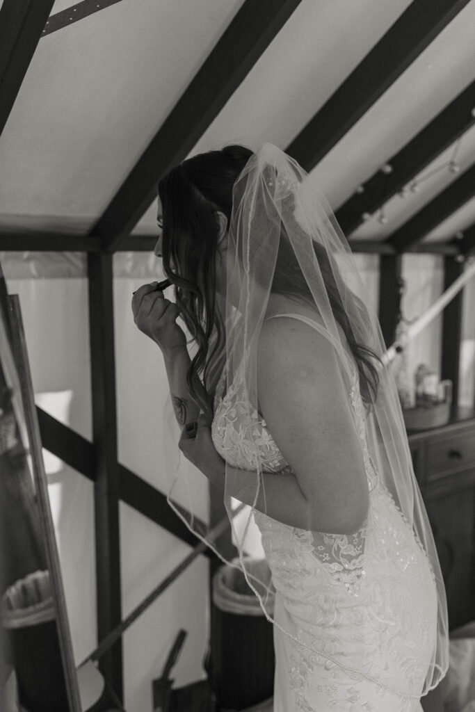 Wedding bride putting lipstick on while looking in mirror at dancing pines