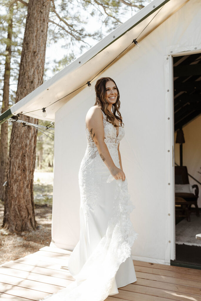 Wedding bride smiling while playing with dress on wooden deck outside canvas cabin at dancing pines