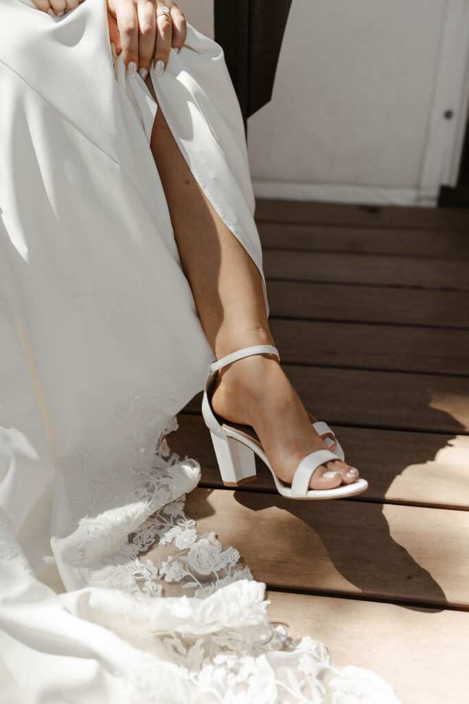 Bride lifting up wedding dress and showing wedding shoes while on wooden deck at dancing pines