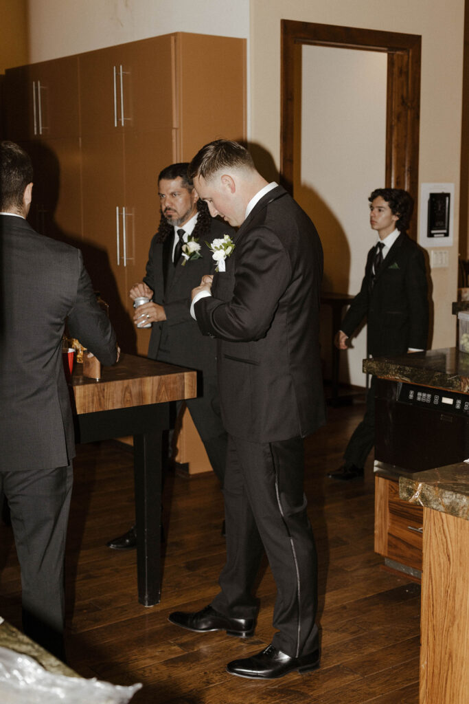 Wedding groom fixing suit jacket while hanging out with groomsmen inside at Aspen Grove