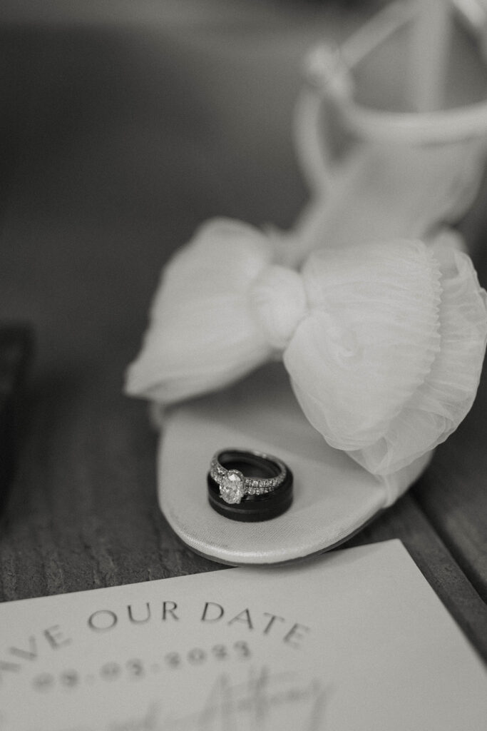 Rings stacked on top of each other on top of wedding shoe next to announcement