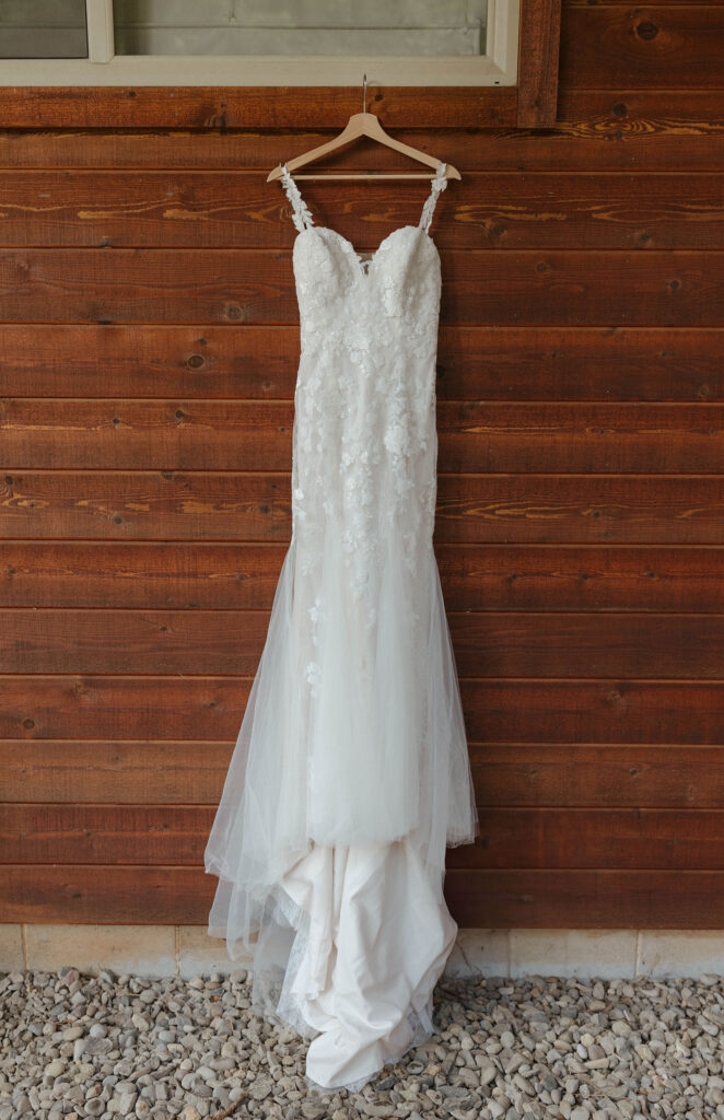 Wedding dress hanging from wooden hanger in front of wooden wall at Aspen Grove