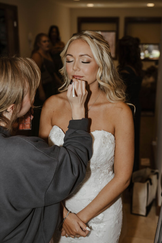 Wedding bride with eyes closed having lipstick put on by makeup artist 