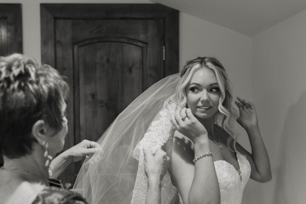 Bride looking over shoulder at mom while she adjusts wedding veil inside at Aspen Grove