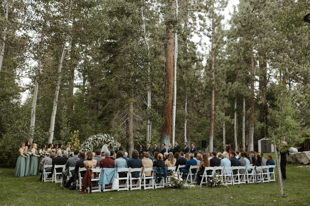 Wedding ceremony overview at Aspen Grove with tall trees and greenery surrounding