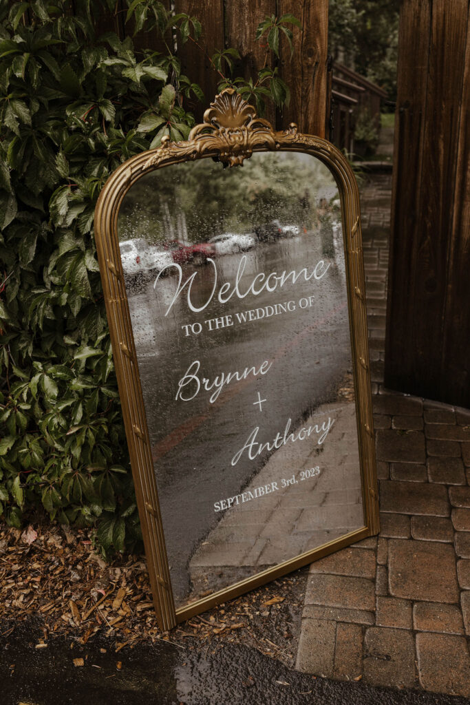 Wedding mirrored welcome sign with couple's name covered in rain drops at Aspen Grove