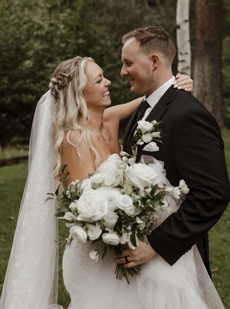 bride and groom smiling with white rose and greenery bouquet