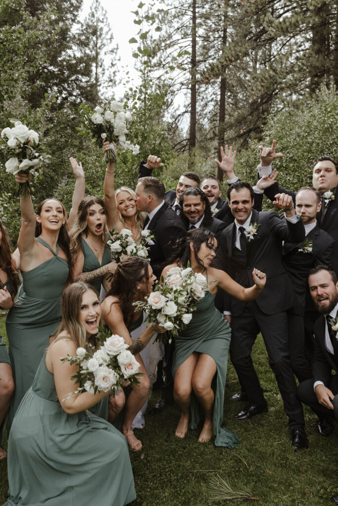 Bridal party celebrating around wedding couple in middle in front of tall trees at Aspen Grove
