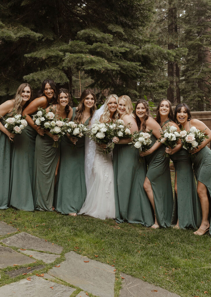 Bride standing on grass with bridesmaids on both sides of her smiling at camera at Aspen Grove