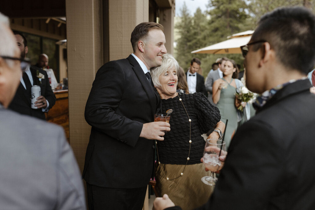 Wedding groom smiling and taking photo with guest while holding a drink on patio at Aspen Grove