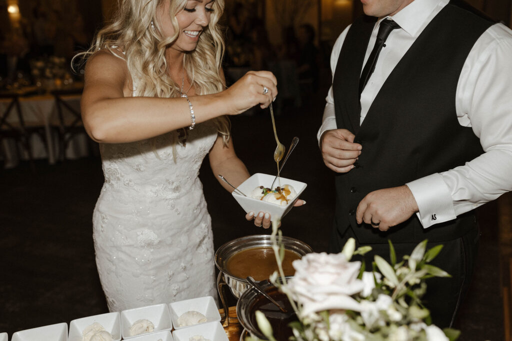 Wedding couple making ice cream sundae together while bride drizzles caramel from spoon inside at Aspen Grove