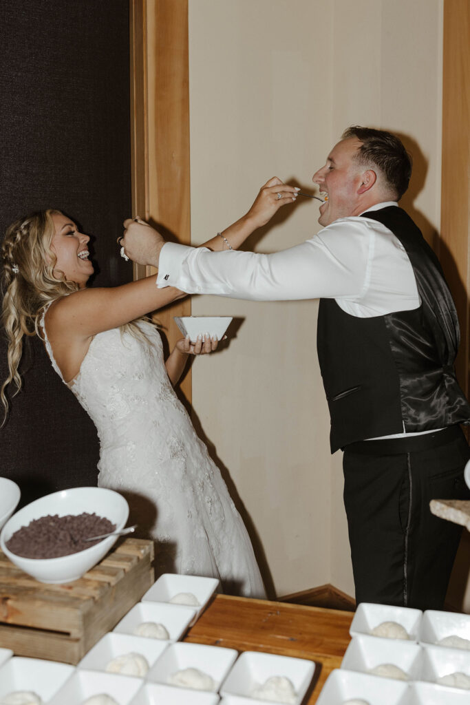 Wedding couple laughing while feeding each other bite of ice cream sundae on spoon inside at Aspen Grove