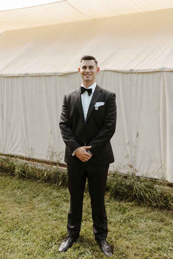 groom smiling outside a tent at his summer wedding at kinship ranch